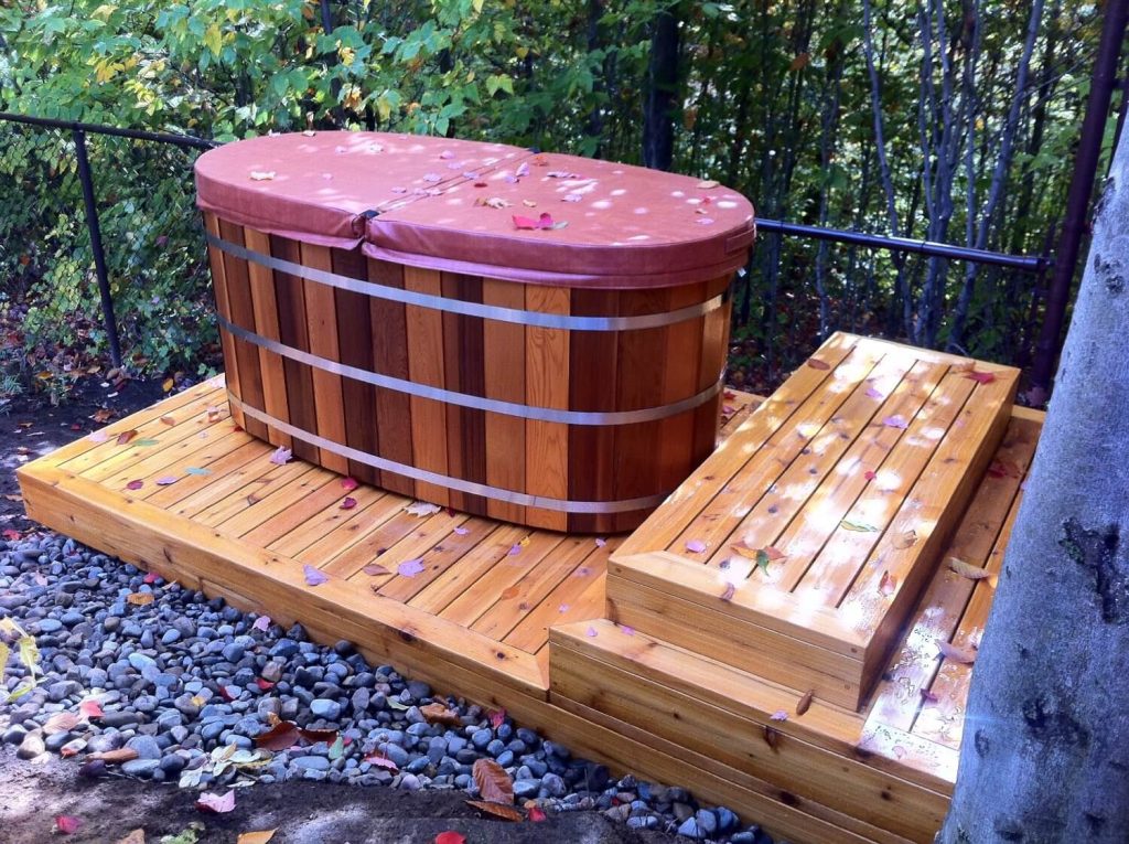 Uma banheira sobre um deque, ambos produzidos com a madeira para área externa de cedro. Ideal para ambientes úmidos.