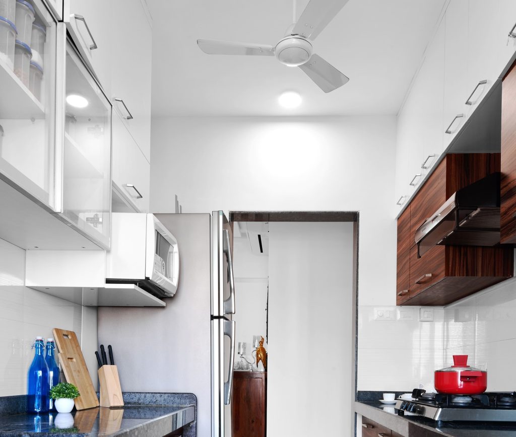 Uma cozinha que possui o tipo de porta basculante nos armários feitos de madeira. Na imagem, vemos um fogão de frente a um balcão e a geladeira ao lado dele.