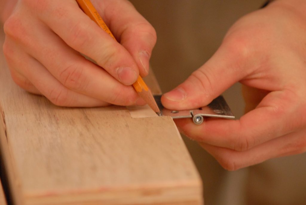 Uma mão segurando um lápis tirando medida de um dos tipos de MDF para fazer seu projeto de marcenaria.