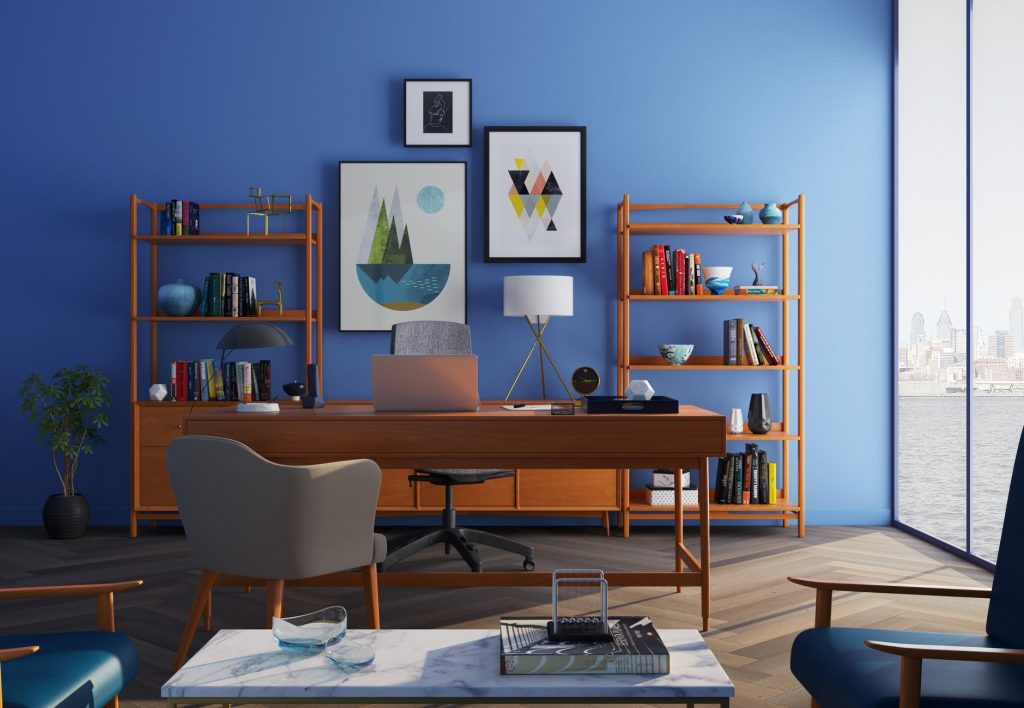 Um escritório com a parede azul, pisos de madeira. Uma mesa e três cadeiras. Atrás da mesa, prateleiras de madeira e alguns quadros na parede. Os elementos foram feitos com diversos tipos de madeira para móveis.
