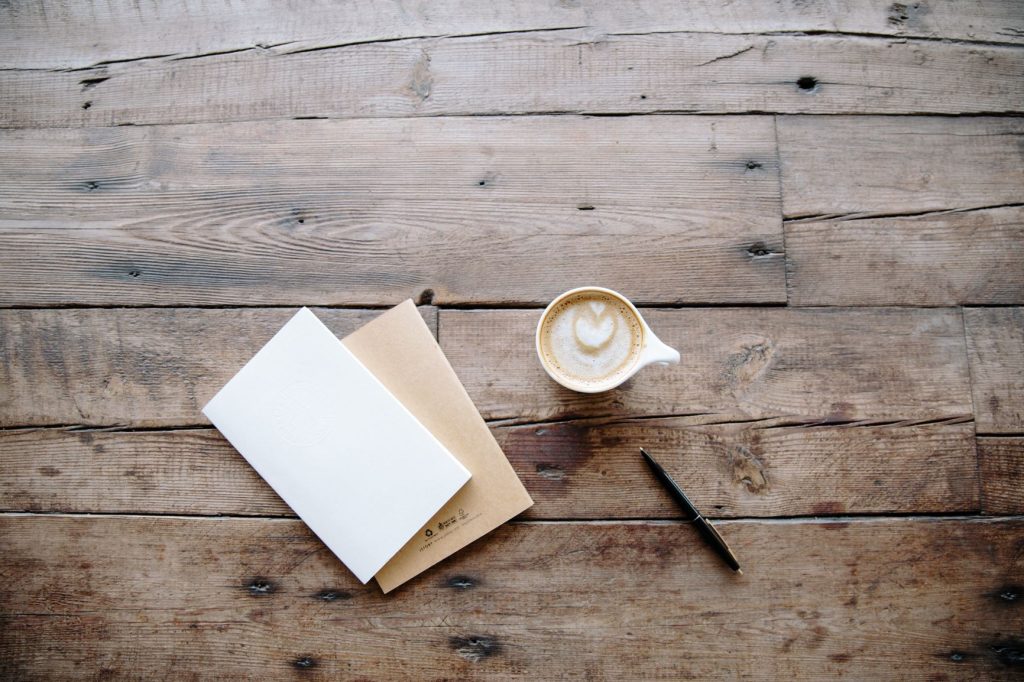uma xícara com leite e café, um bloco de anotações e uma caneta sobre uma superfície de madeira, preparada por alguém que entende como limpar madeira