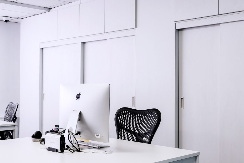 Um escritório com um grande armário branco de madeira, com um tipo de porta de correr, duas mesas, cadeiras e macbooks