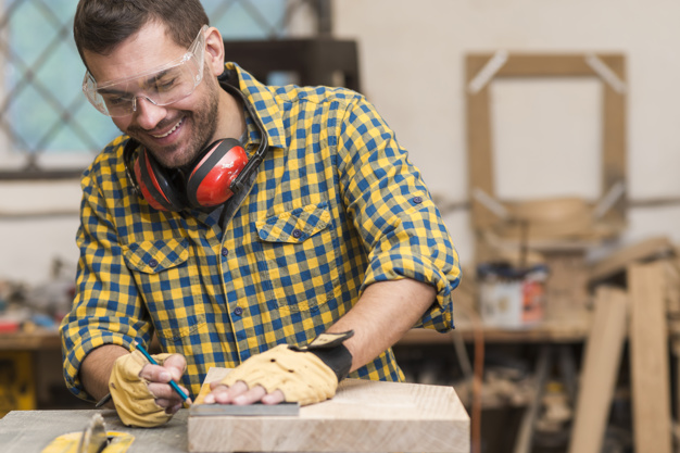 Um marceneiro sorrindo, pois entende a importância da segurança do trabalho. Ele está fazendo um projeto com equipamentos de segurança .
